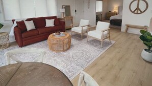 A spacious living area with a red sofa, white armchairs, a round wicker coffee table, and a large window. - Summerland Ocean View no. 3 (Summerland)