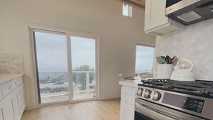 A modern kitchen with a large stove, white cabinets, and a view through the sliding glass door. - Summerland Ocean View no. 3 (Summerland)