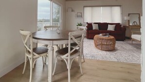 A spacious room with a high ceiling, wooden beams, a dining table with chairs, a red sofa, and a wicker coffee table. - Summerland Ocean View no. 3 (Summerland)