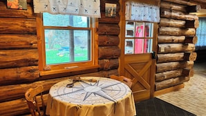 A log cabin interior with a round table, wooden walls, a window with a view, and a door with a curtain. - Authentic log cabin! (Youngstown)