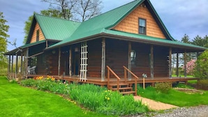 A log cabin with a green metal roof, a porch with a ladder, and a gravel driveway. - Authentic log cabin! (Youngstown)
