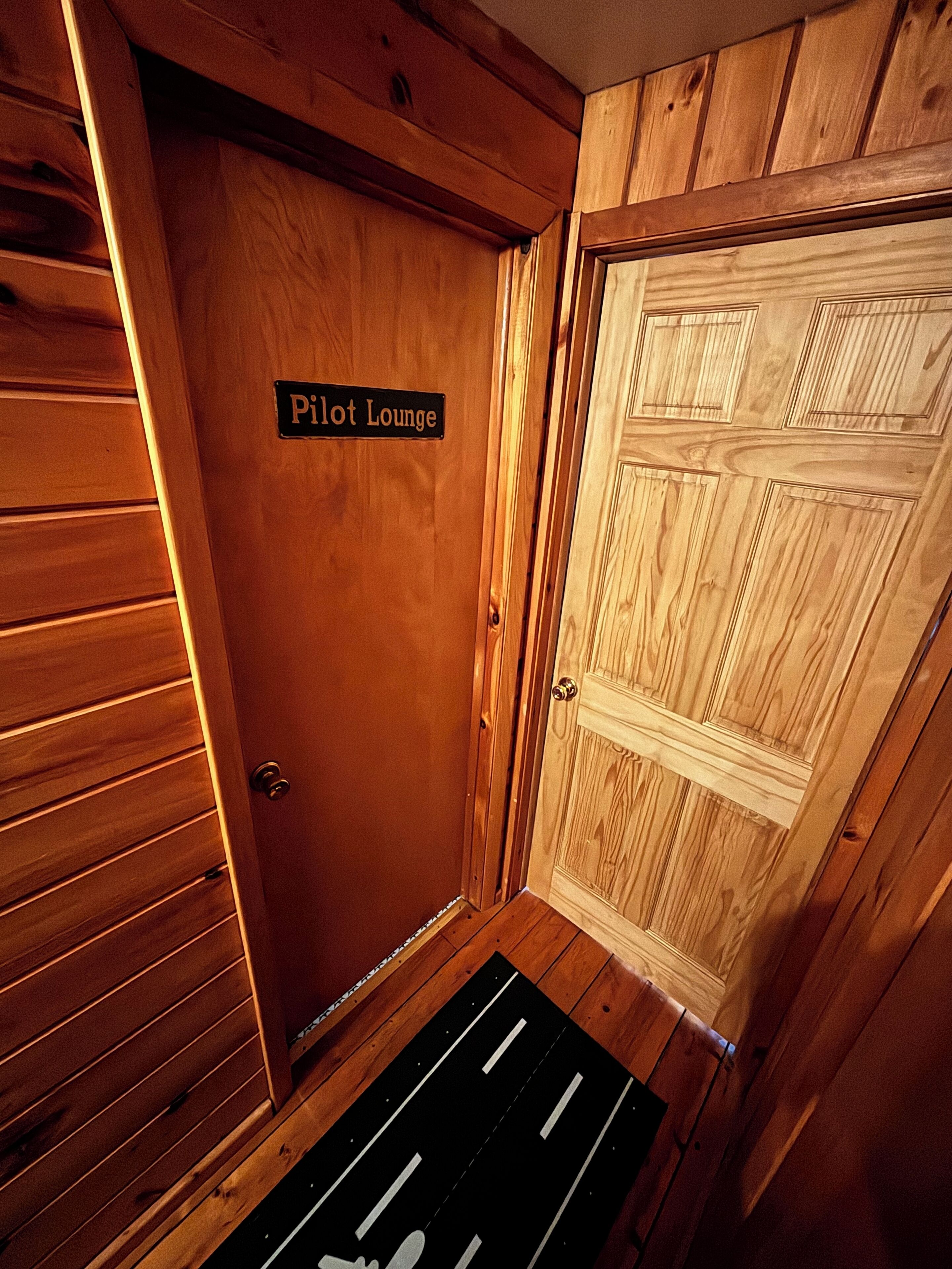 Una porta de fusta amb la inscripció 'Pilot Lounge' i un felpú de colors negre i blanc.