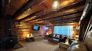 A log cabin interior with a fireplace, leather sofa, and a television mounted on the wall. - Authentic log cabin! (Youngstown)