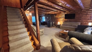 A log cabin interior with a staircase, a living room with a sofa and a coffee table, and a fireplace. - Authentic log cabin! (Youngstown)