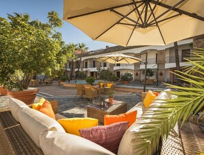 An outdoor patio area with wicker furniture, yellow cushions, and a large umbrella.