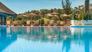 A swimming pool with lounge chairs and umbrellas, surrounded by greenery and buildings. - Precioso Apartamento EN Planta Baja A Estrenar (MIJAS-COSTA)