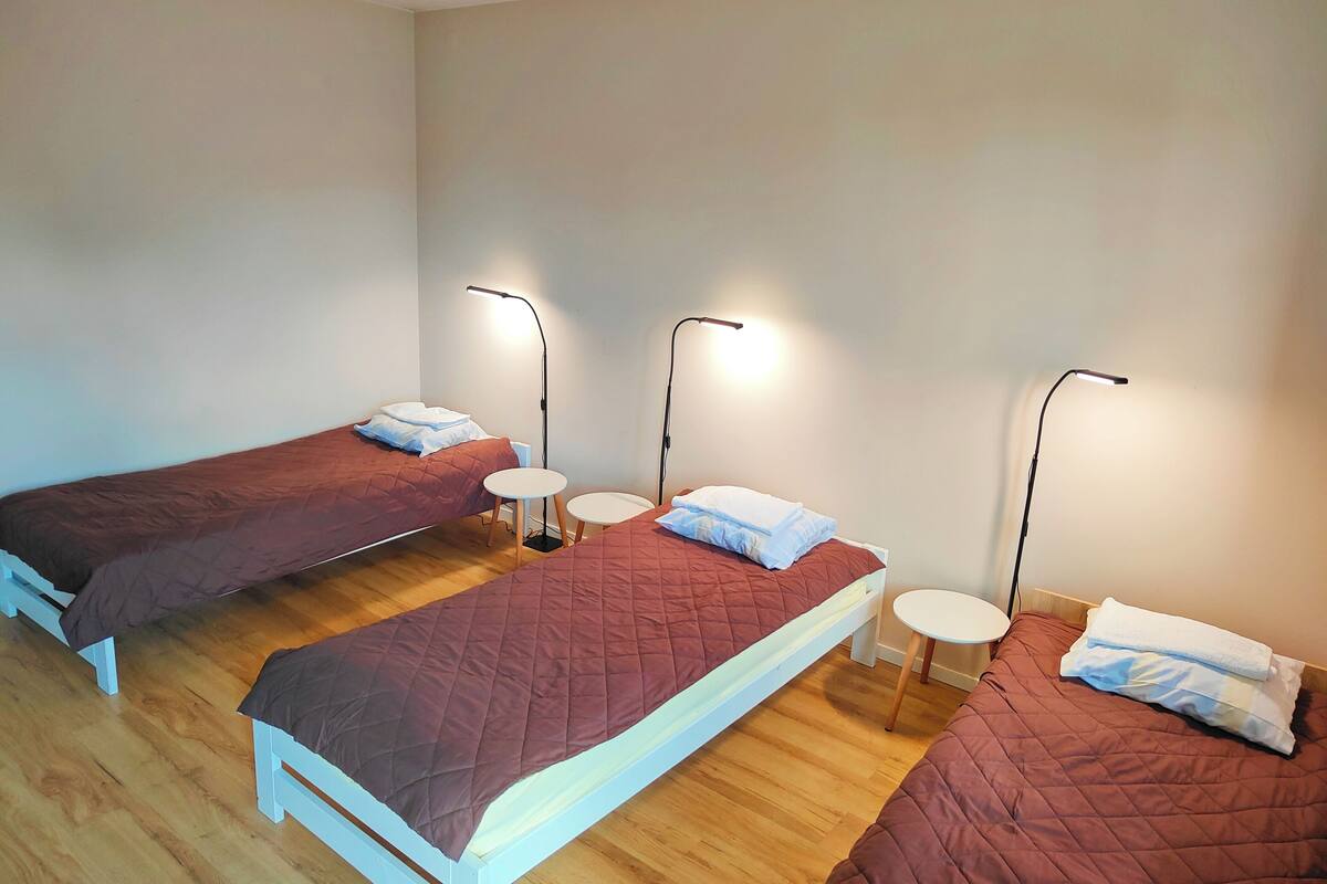 A room with three beds, each with a bedside table and a lamp.