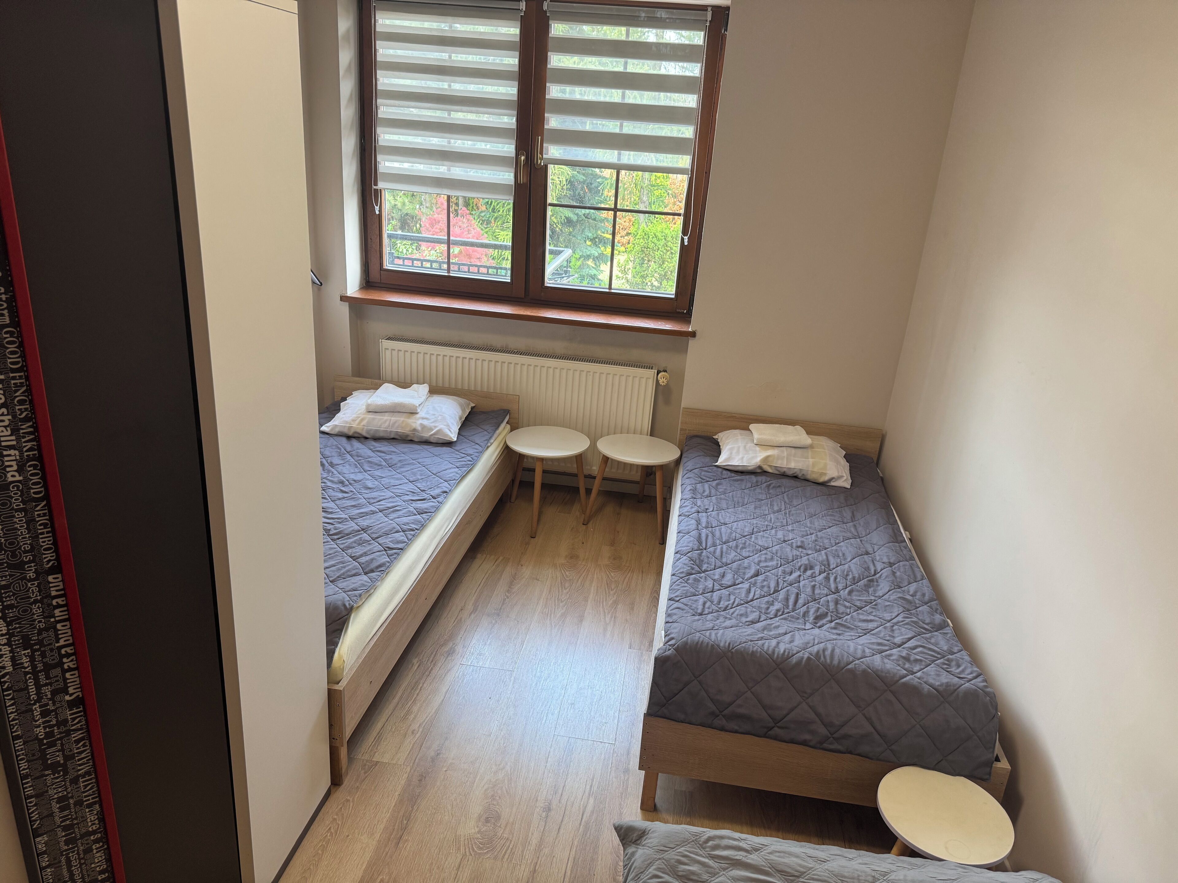 A small, narrow room with two single beds, a small table, and a radiator.