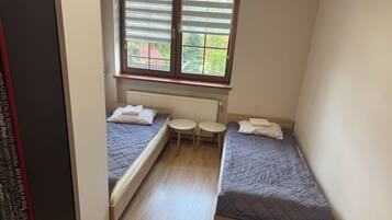 A small, narrow room with two single beds, a small table, and a radiator.