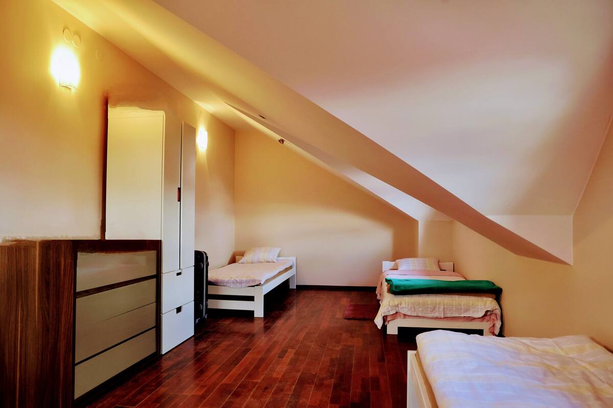 A small, cozy attic bedroom with two single beds, a wooden dresser, and a door leading to another room.