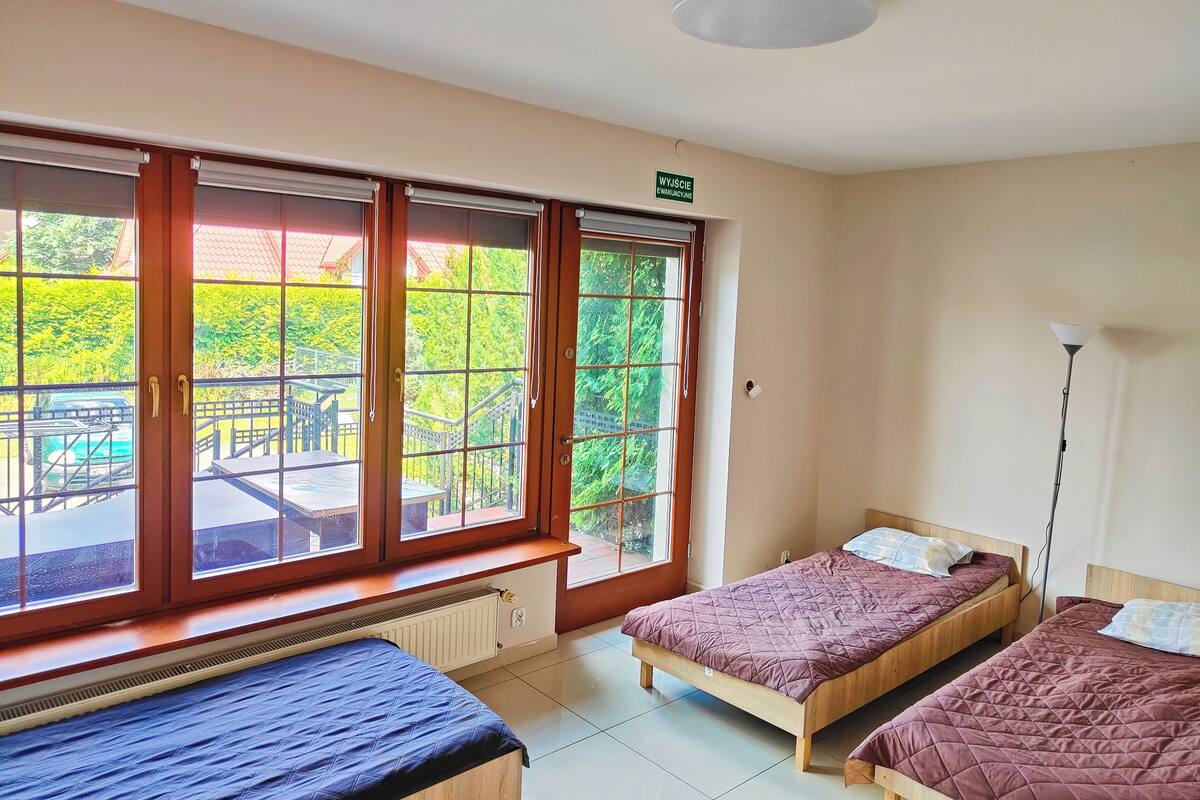 A room with two beds, large windows, a radiator, and a ceiling light.