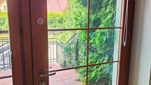 Une porte en bois ornée d’un motif en croisillons, donnant sur un balcon dont le sol est recouvert de carreaux et qui est protégé par une rambarde en métal.