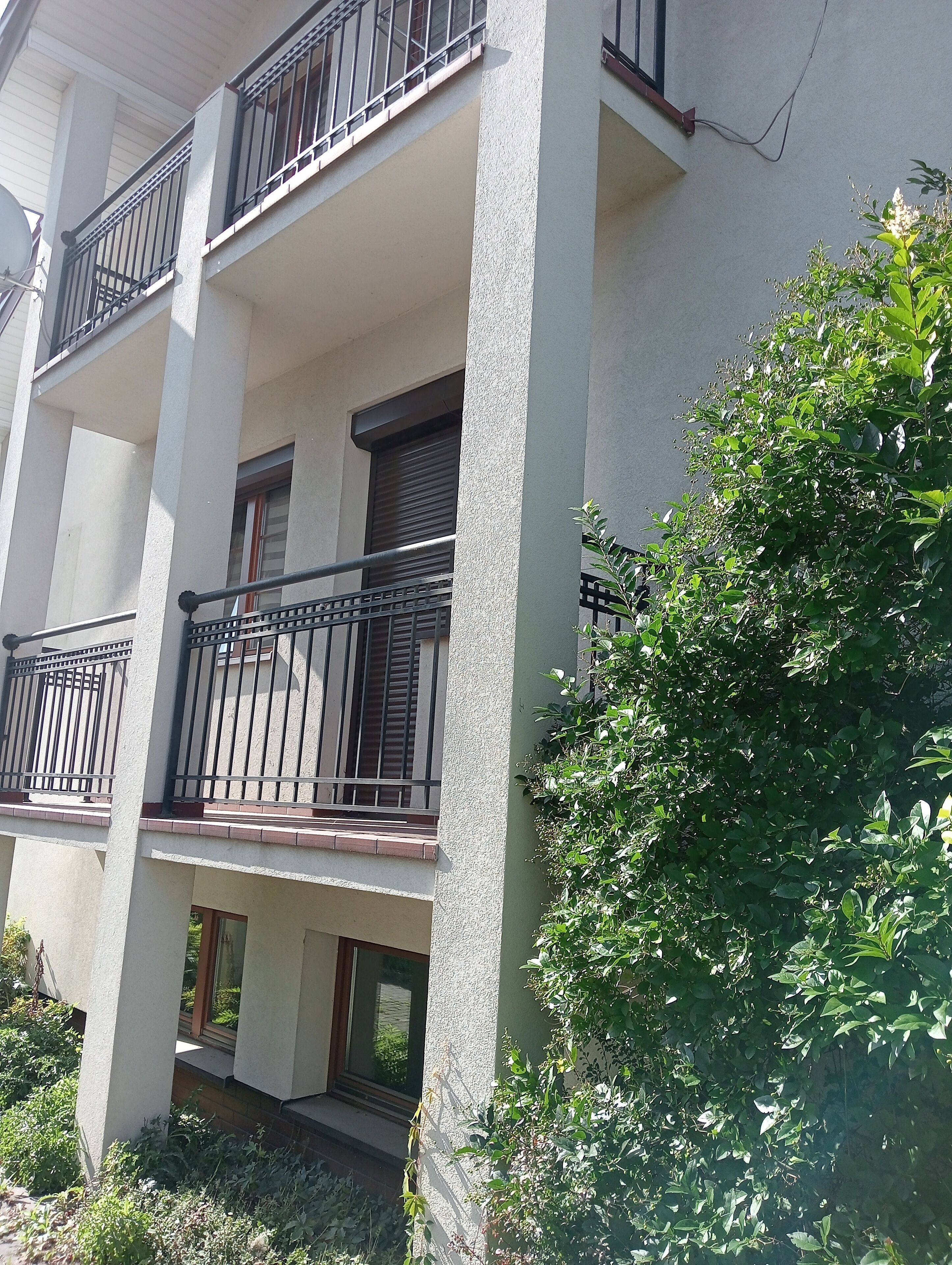 A multi-story building with balconies, large windows, and a garden area.