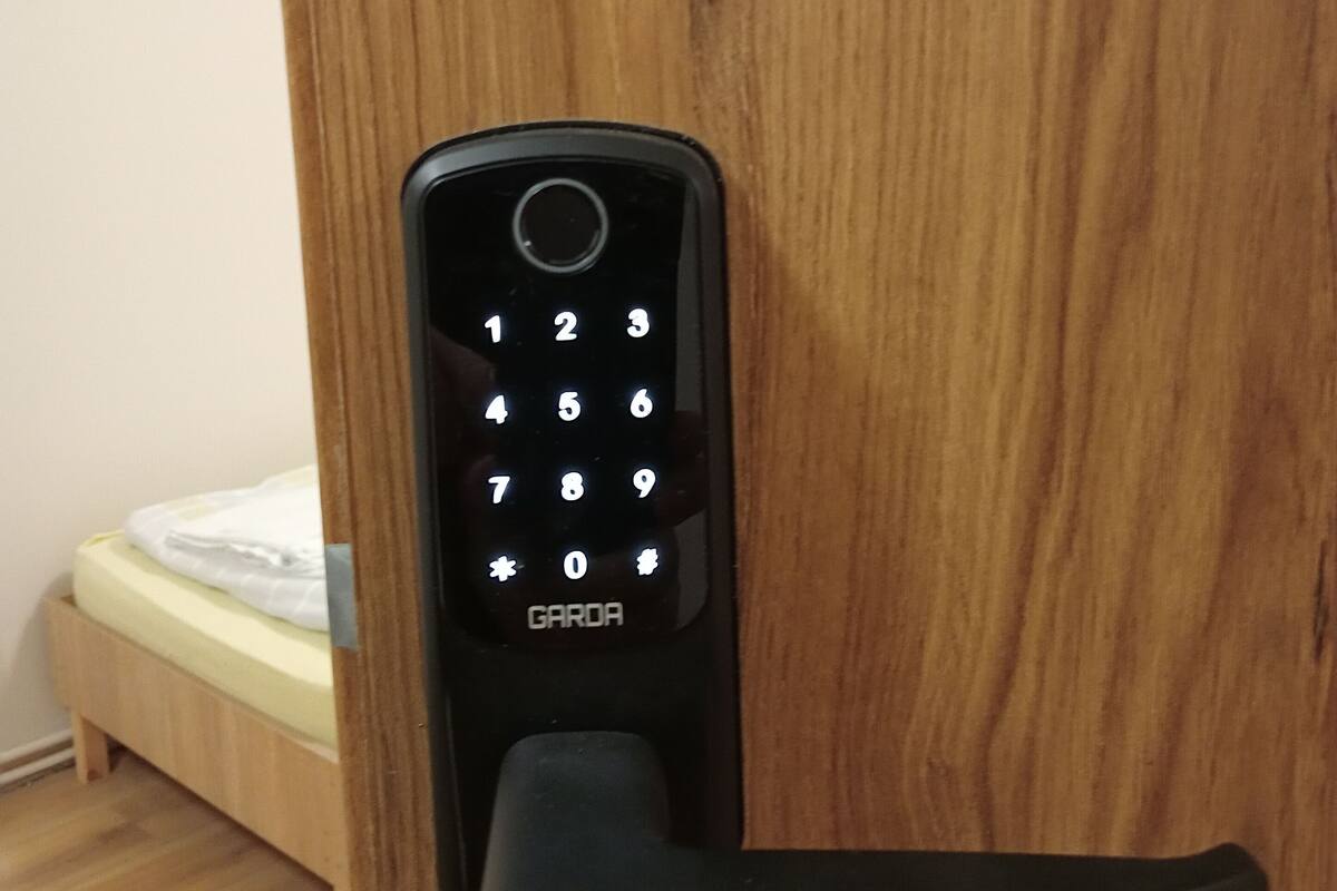 A black GARDA door lock with a numeric keypad, installed on a wooden door.