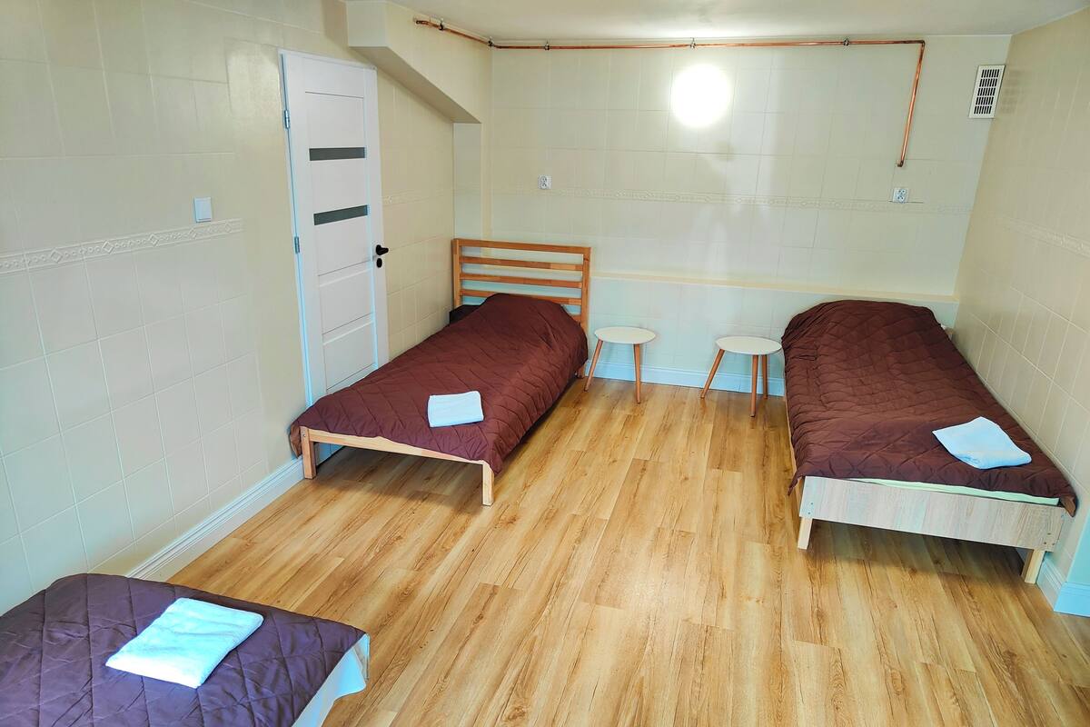 A small, single-room accommodation with two wooden beds, a small table, and a wardrobe.