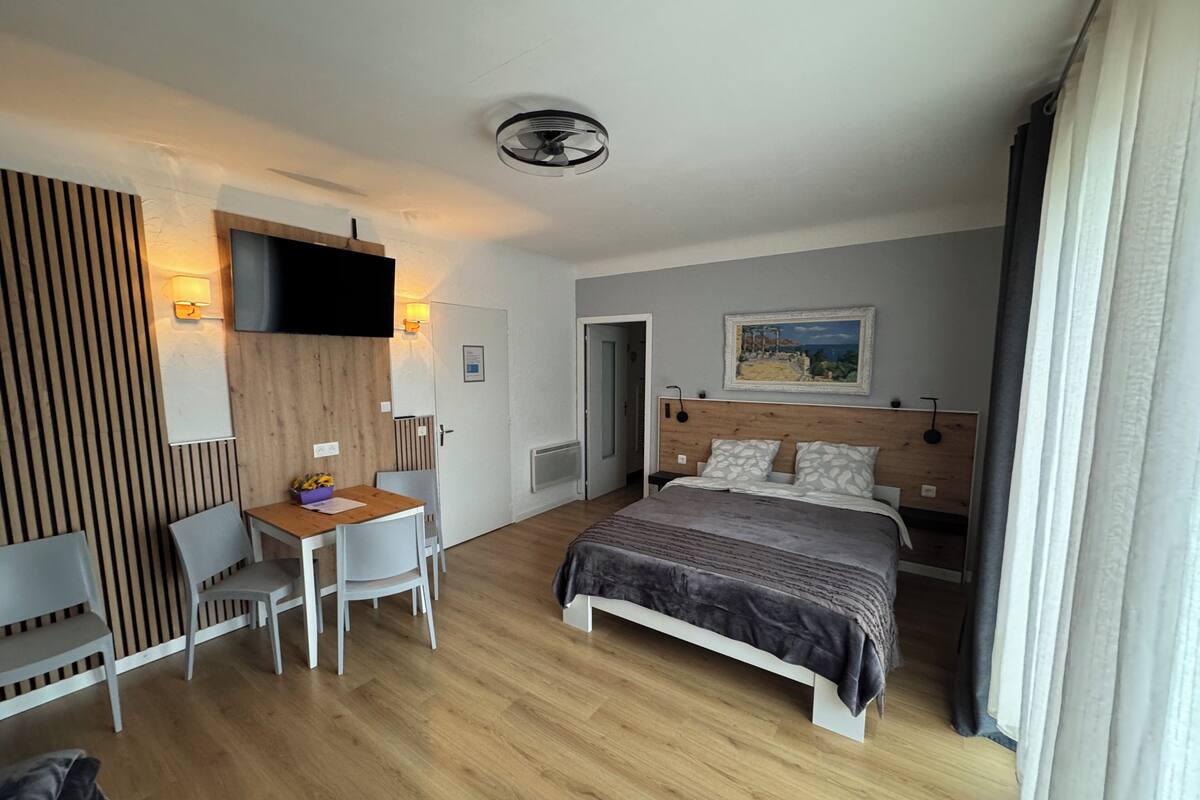 A hotel room with a bed, a desk, a chair, a TV, and a painting on the wall.