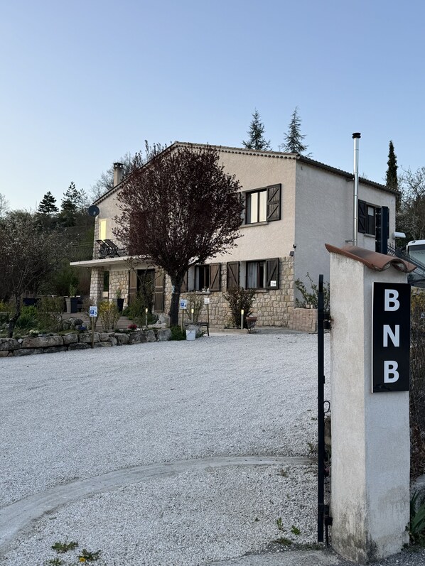 Un bâtiment à deux étages avec une façade en pierre, une allée gravillonnée et une enseigne indiquant « BNB ».