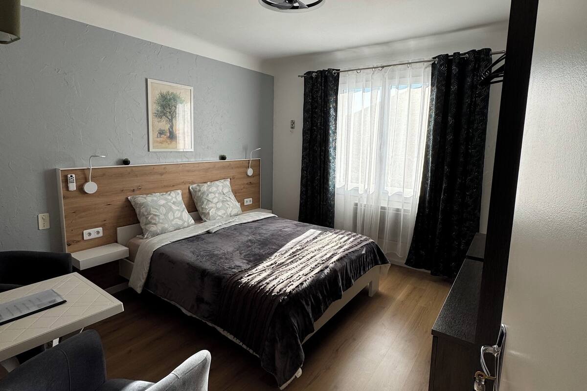 A modern hotel room with a bed, a desk, a chair, and a wardrobe.