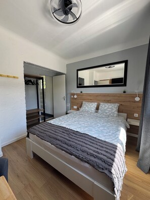 Une chambre moderne avec une tête de lit en bois, un grand lit recouvert d’une couvre-lit à motifs, une table de chevet avec une lampe et un miroir accroché au mur.
