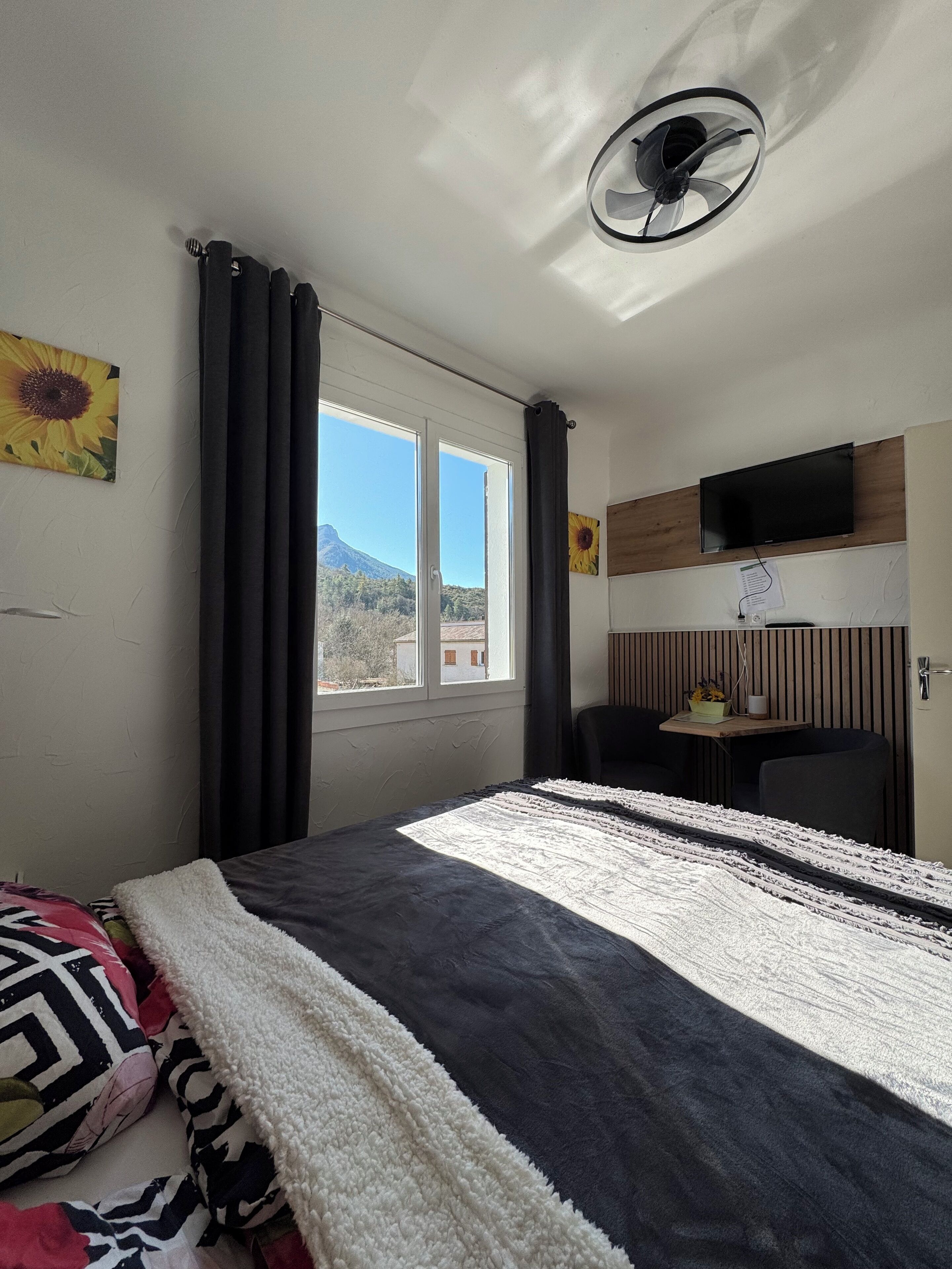 Un dormitorio con cama, televisor, ventana con cortinas y vista al exterior.