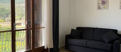 Ein Schlafzimmer mit einem Bett, einer dunklen Couch und einem großen Fenster mit Vorhängen.