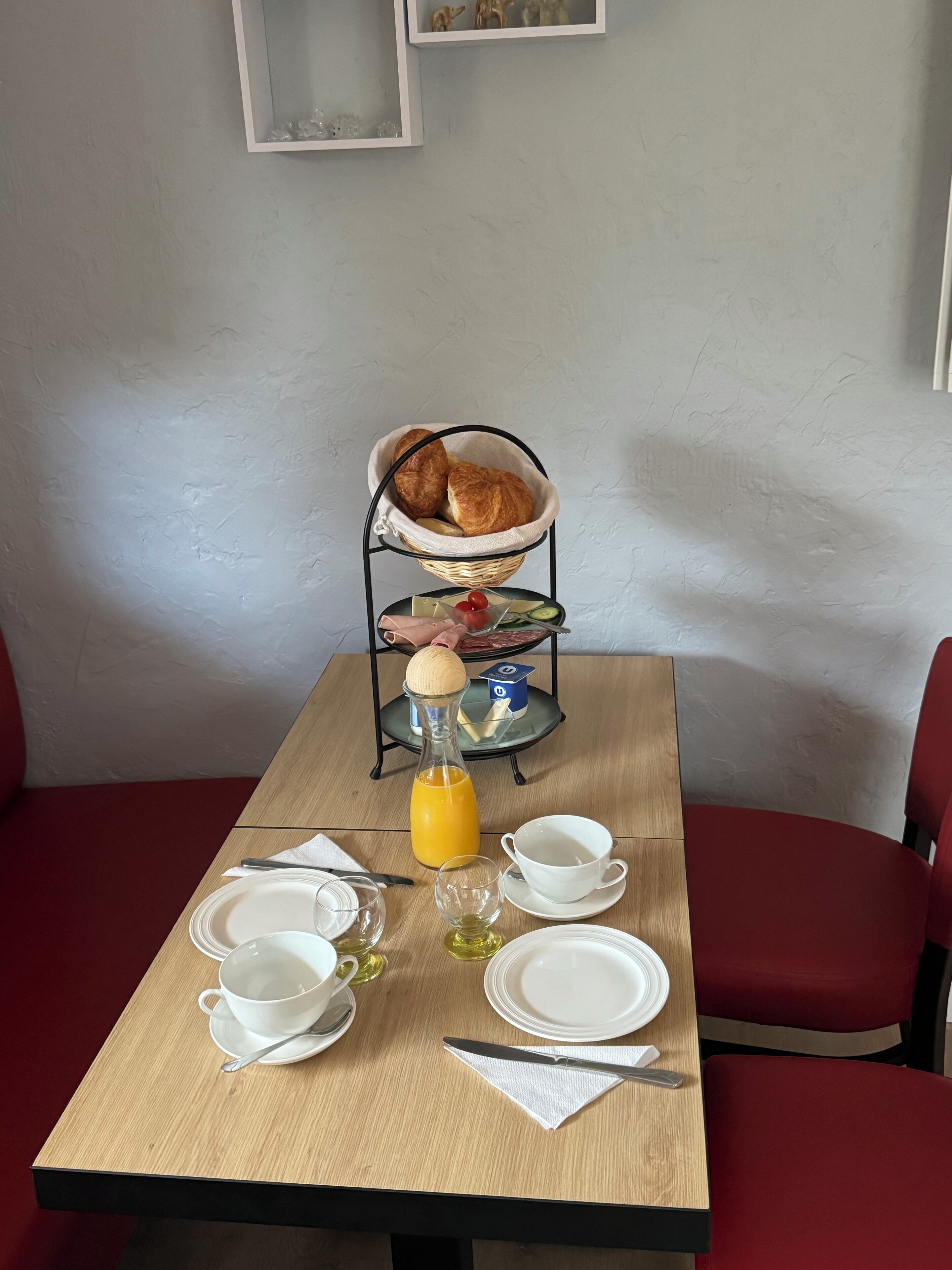 A breakfast table set with plates, cups, a knife, a bottle of orange juice, and a basket of croissants.