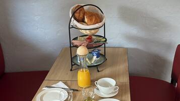 A breakfast table set with plates, cups, a knife, a bottle of orange juice, and a basket of croissants.