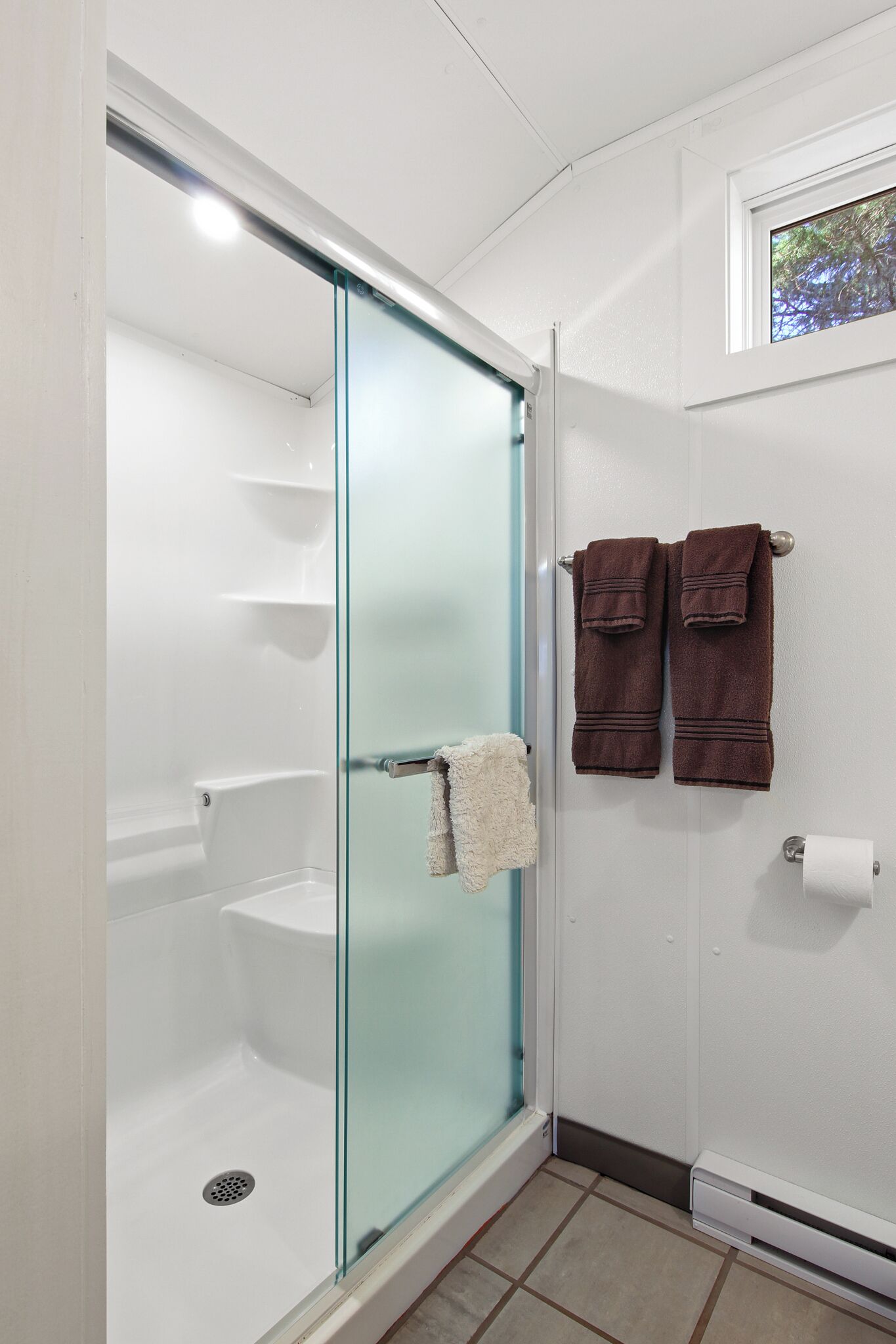 A bathroom with a glass shower enclosure, a white toilet, and two towels hanging on the wall.