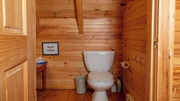 A wooden cabin bathroom with a toilet, a trash can, and a sign that reads 'Beach Towels'.