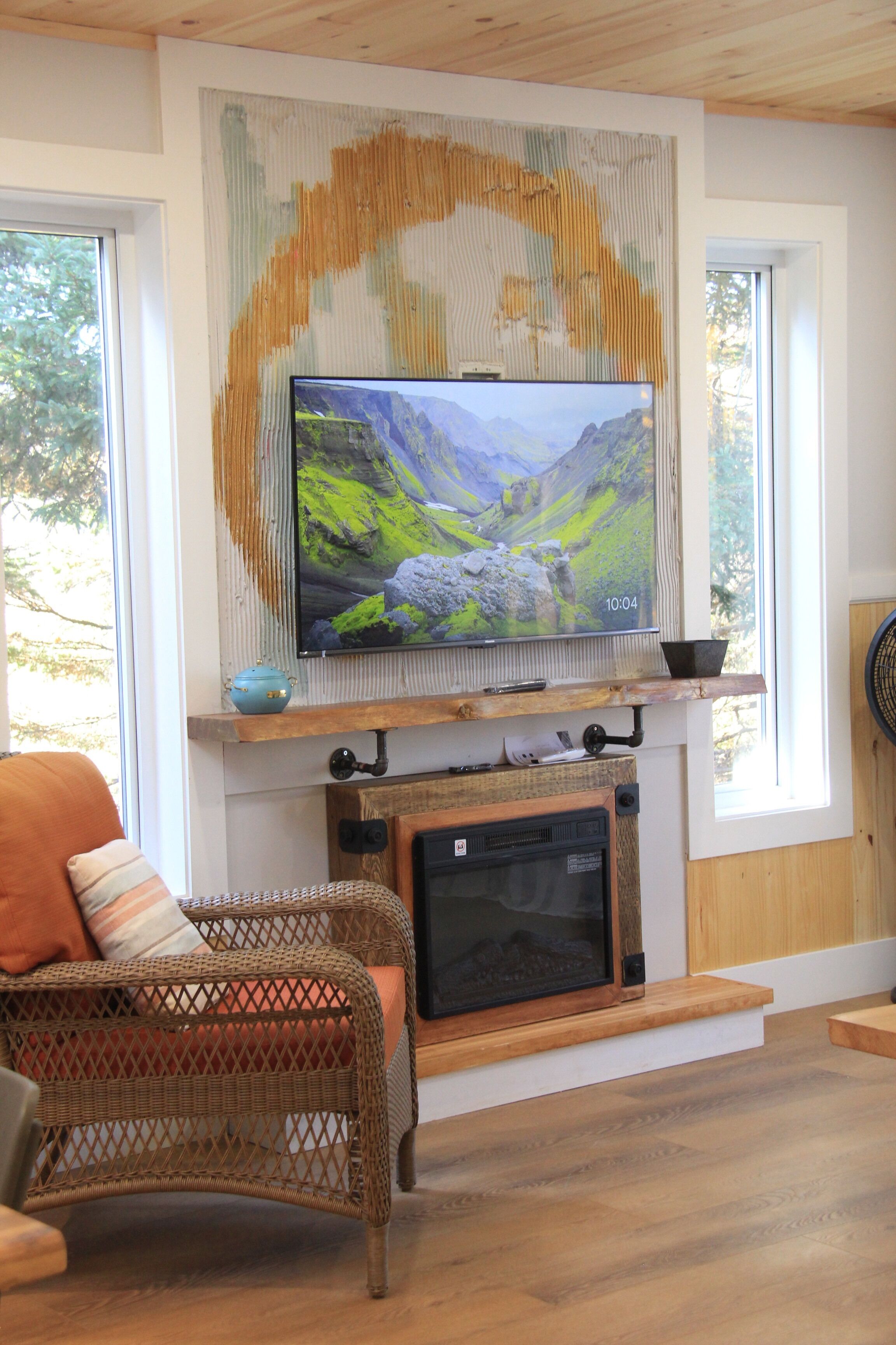 Una sala de estar con un televisor montado en la pared, una chimenea abajo y un sillón de mimbre con cojines.