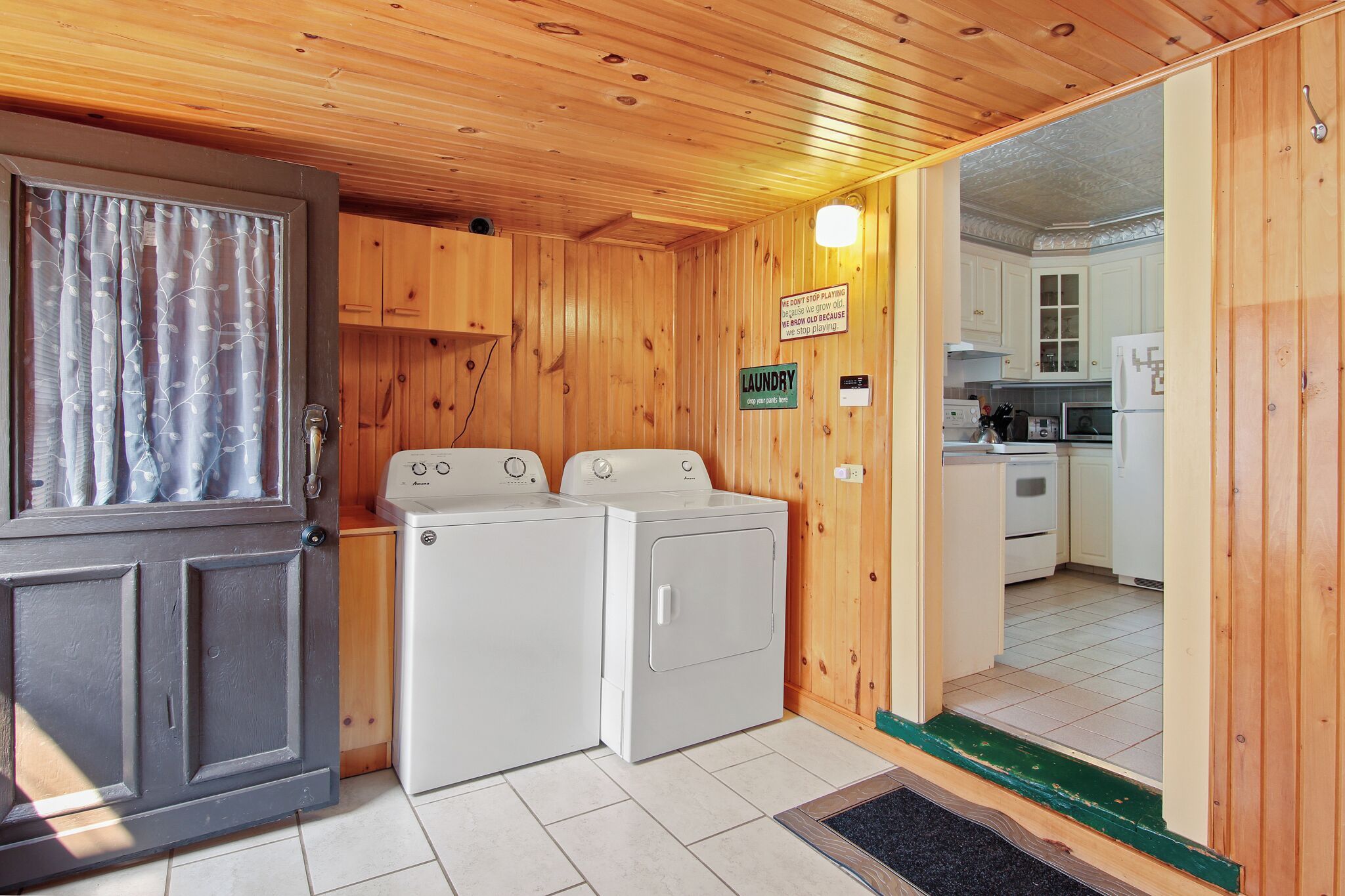 A laundry area with two washing machines, a sign indicating the location, and a view into a kitchen with white cabinets and appliances.