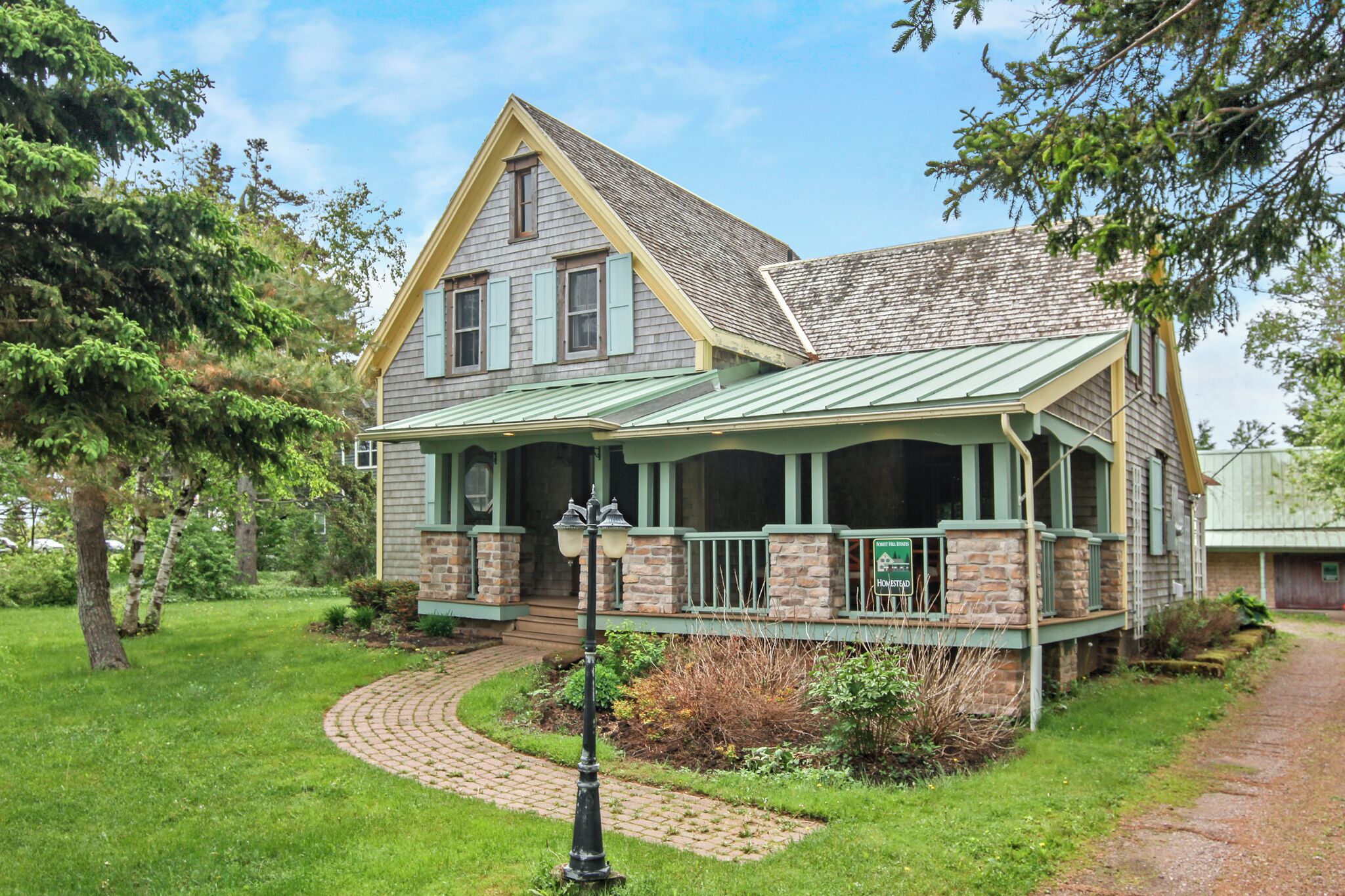 A two-story house with a green roof, a front porch, and a brick foundation.