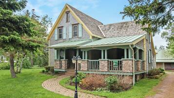 A two-story house with a green roof, a front porch, and a brick foundation.