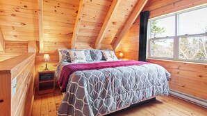 A wooden cabin bedroom with a bed, nightstands, and a window. - Avonlea Forest Hill Cottages (Cavendish)