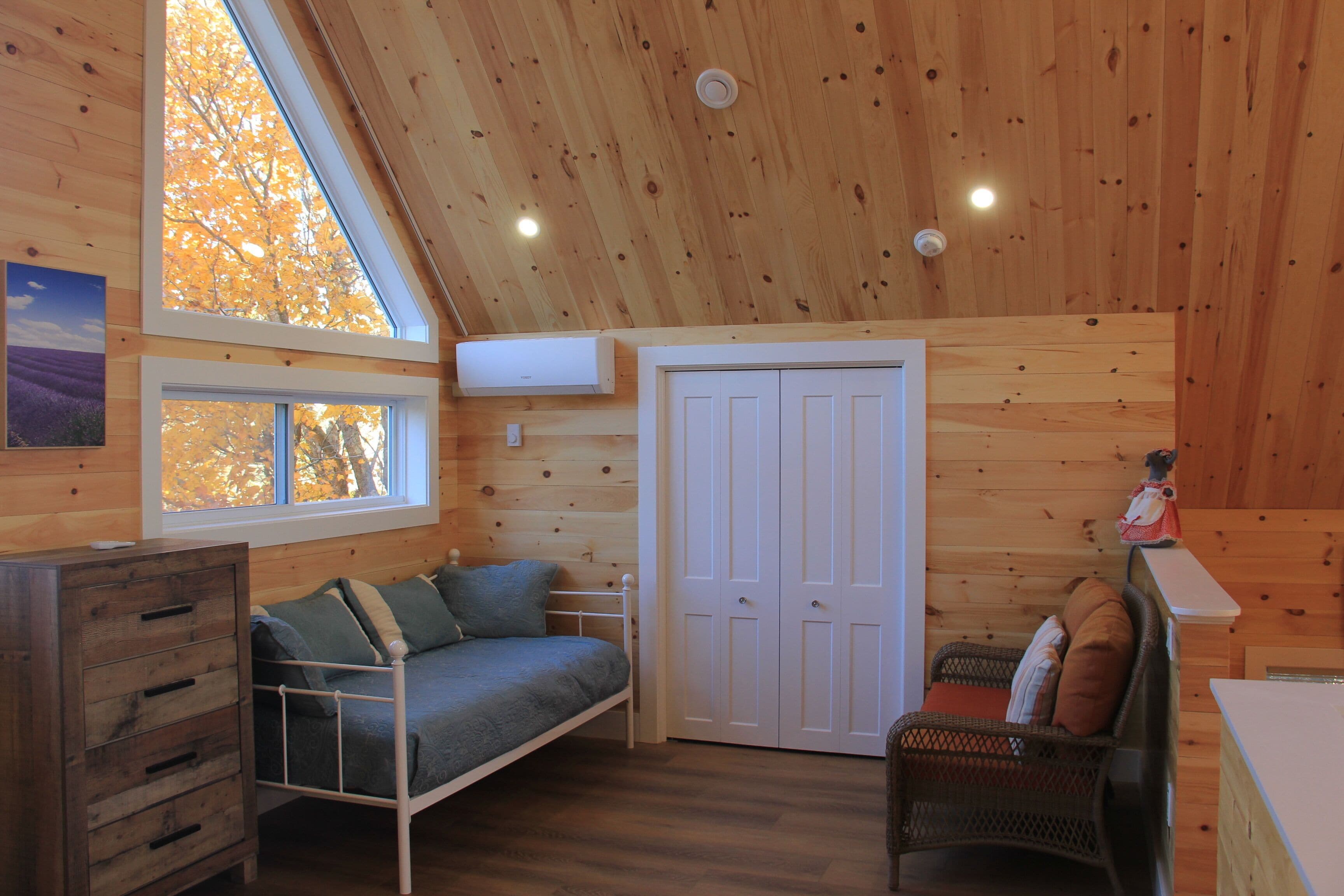 Een gezellig chaletinterieur met een slaapzolder, een kleine bank, een rieten stoel en een houten dressoir.