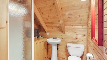 A small, wooden cabin bathroom with a white sink, toilet, and wooden cabinets.