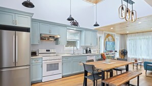 A modern kitchen with light blue cabinets, stainless steel appliances, and a wooden dining table with benches. - Avonlea Forest Hill Cottages (Cavendish)