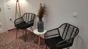 A room with two black wireframe chairs, a small round table, a tall floor lamp, and a vase with dried plants. - Flora Rooms and Apartments Paros (Paros)