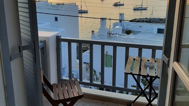 A balcony with a view of boats on the water, a table, and a chair. - Flora Rooms and Apartments Paros (Paros)