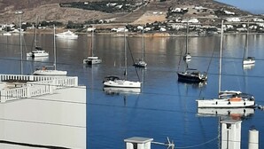 A marina with boats docked, a mountain in the background, and a white building with a balcony in the foreground. - Flora Rooms and Apartments Paros (Paros)
