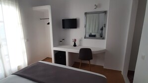 A hotel room with a bed, a desk, a chair, a television, and a mirror. - Flora Rooms and Apartments Paros (Paros)