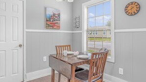 A dining area with a wooden table, chairs, a painting, a clock, and a window with a view. - Close to Hospital and Downtown, Eastside Bungalow, Dogs Welcome + Fee (Florence)