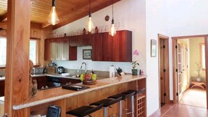 Une cuisine avec des meubles de rangement en bois, un coin bar avec des tabourets et des luminaires suspendus.
