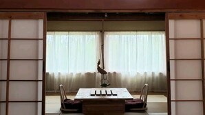 Une pièce de style japonais traditionnel, avec un sol recouvert de tatamis, une petite table et une cage à oiseaux suspendue, ainsi que des paravents shoji.