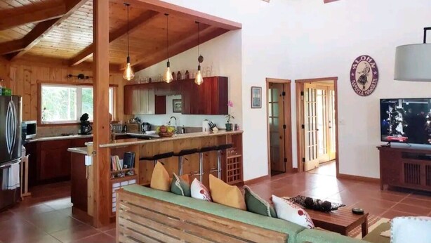 Un vaste espace de vie doté d’un plafond en bois, d’une cuisine avec un bar et d’un téléviseur.