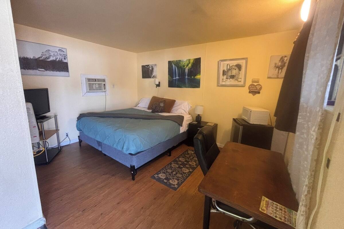 Una habitación pequeña y funcional con cama, escritorio, silla, televisor y microondas.