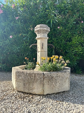 Una jardinera de concreto con un pilar de piedra, rodeada de grava y plantas florecientes.