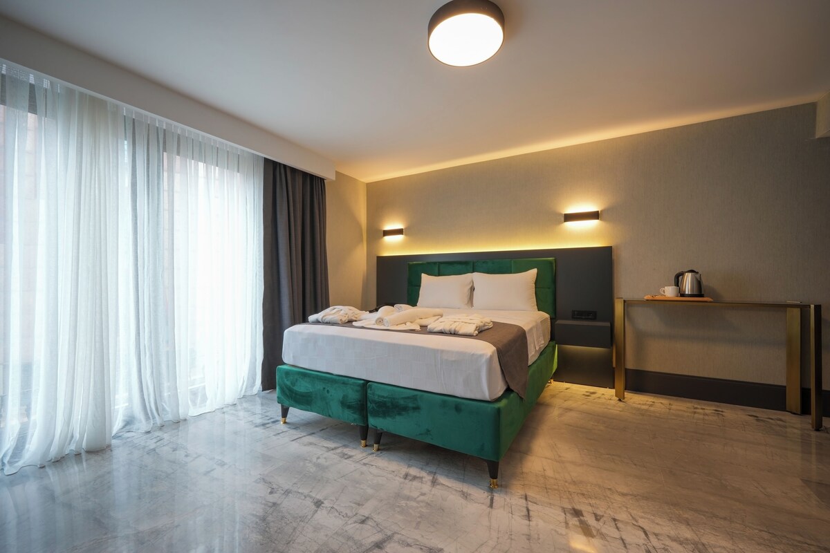 Habitación de hotel moderna con una cama grande, una mesita de noche y vistas a la ciudad.