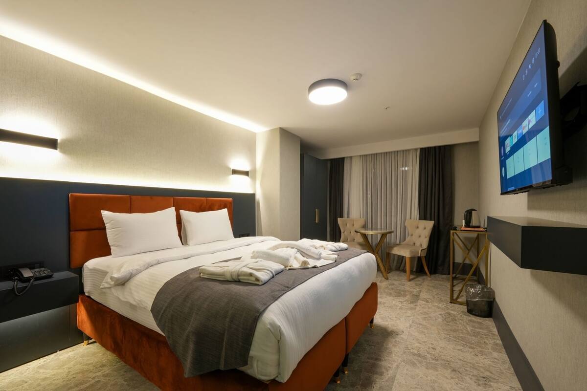 Una habitación de hotel con cama, mesita de noche, lámpara, televisor y una pequeña mesa con sillas.
