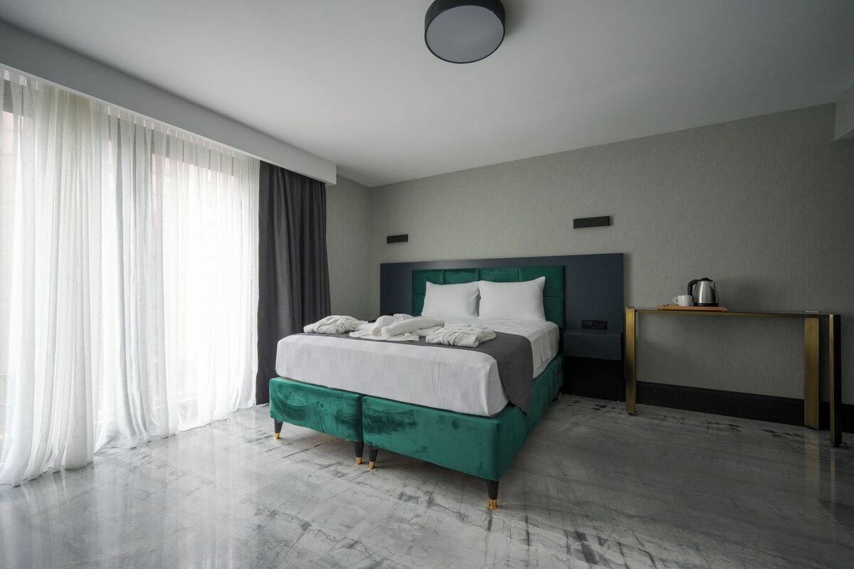Una habitación de hotel moderna con una cama grande, una mesita de noche y vistas a la ciudad.